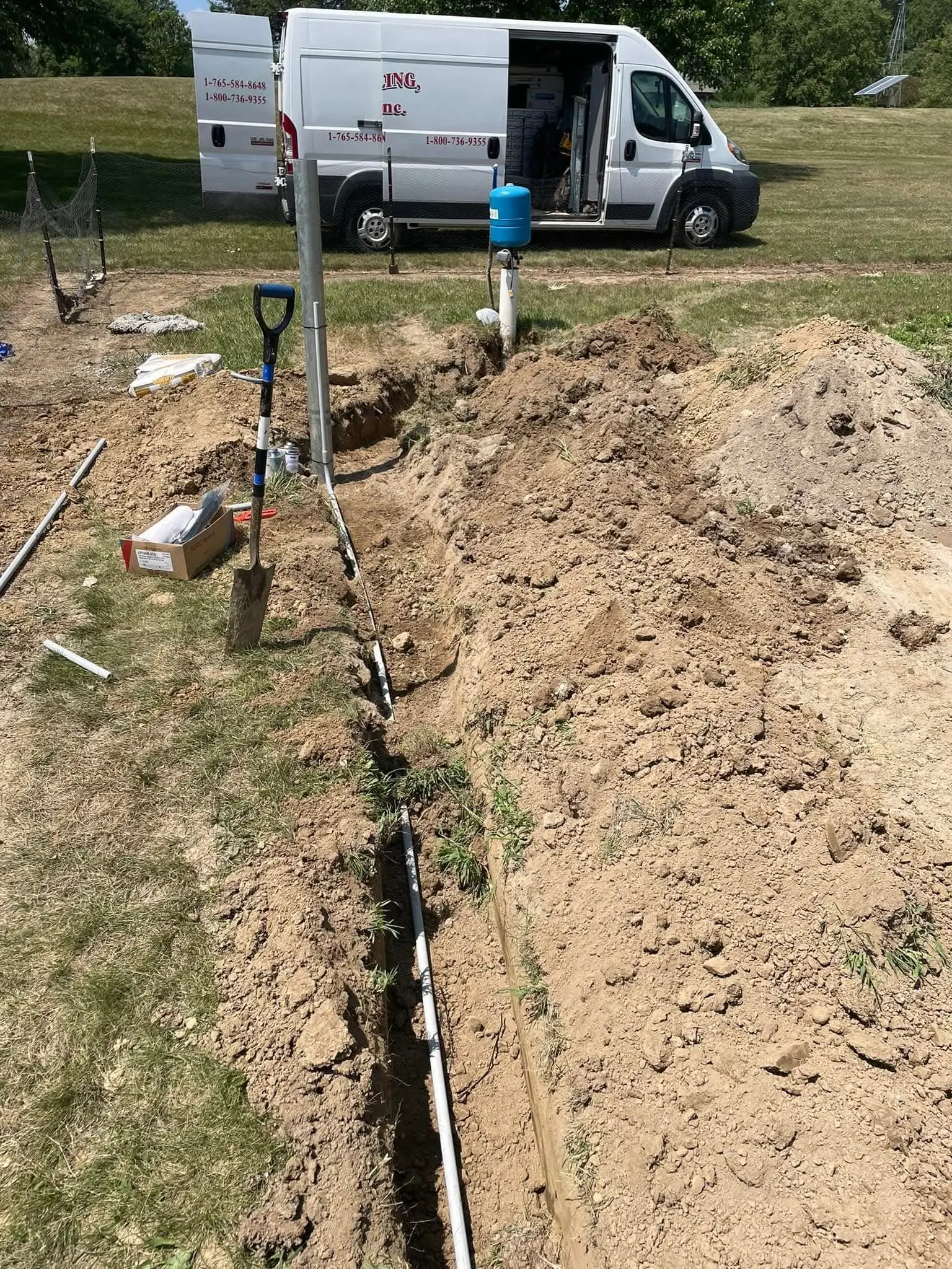 A Wiley Well Drilling service van beside an open trench with a newly installed water line and pressure tank.